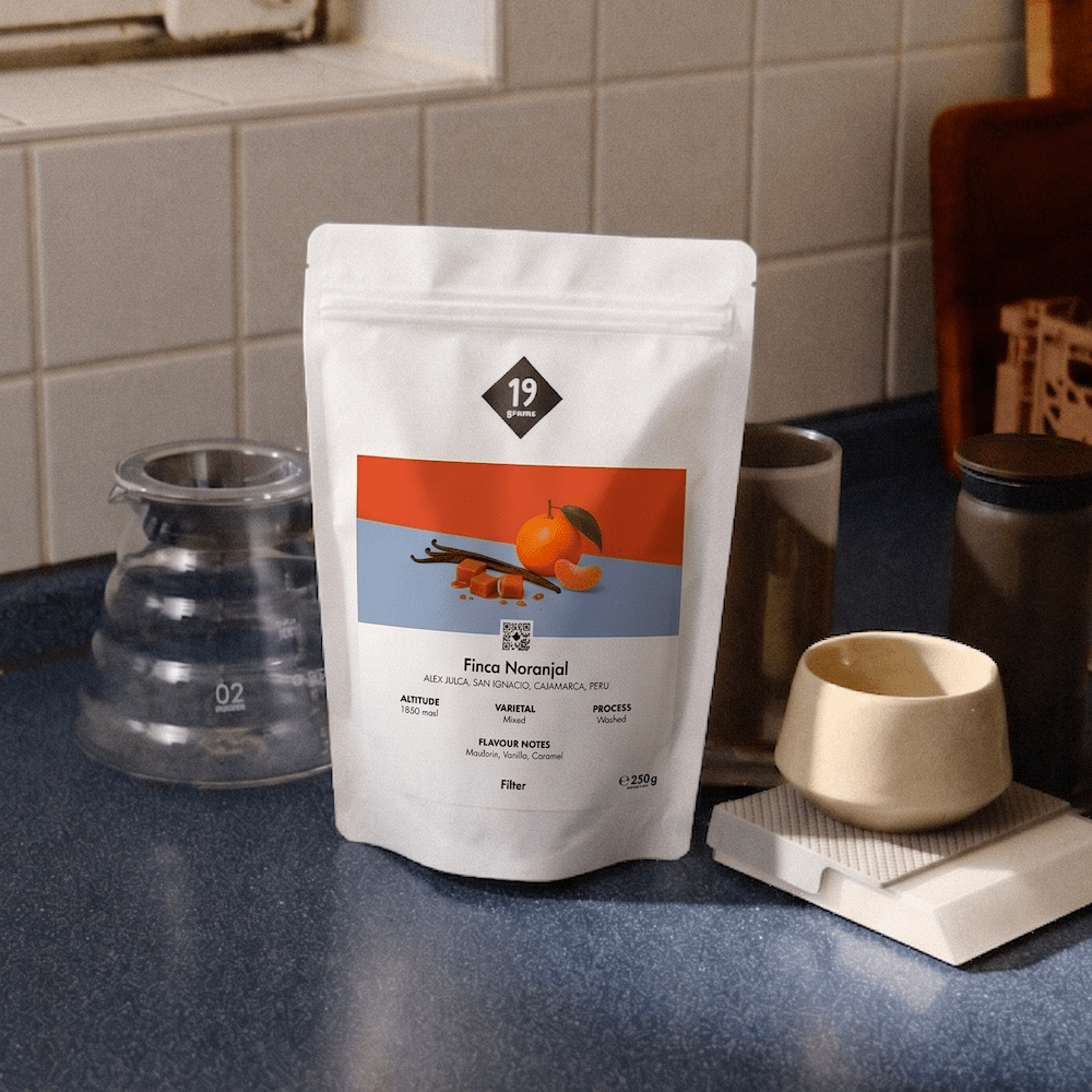 19grams Finca Naranjal Filter Kaffeebeutel neben Glaskaraffe und Keramiktasse auf blauem Tresen – Specialty Coffee Peru Moodshot