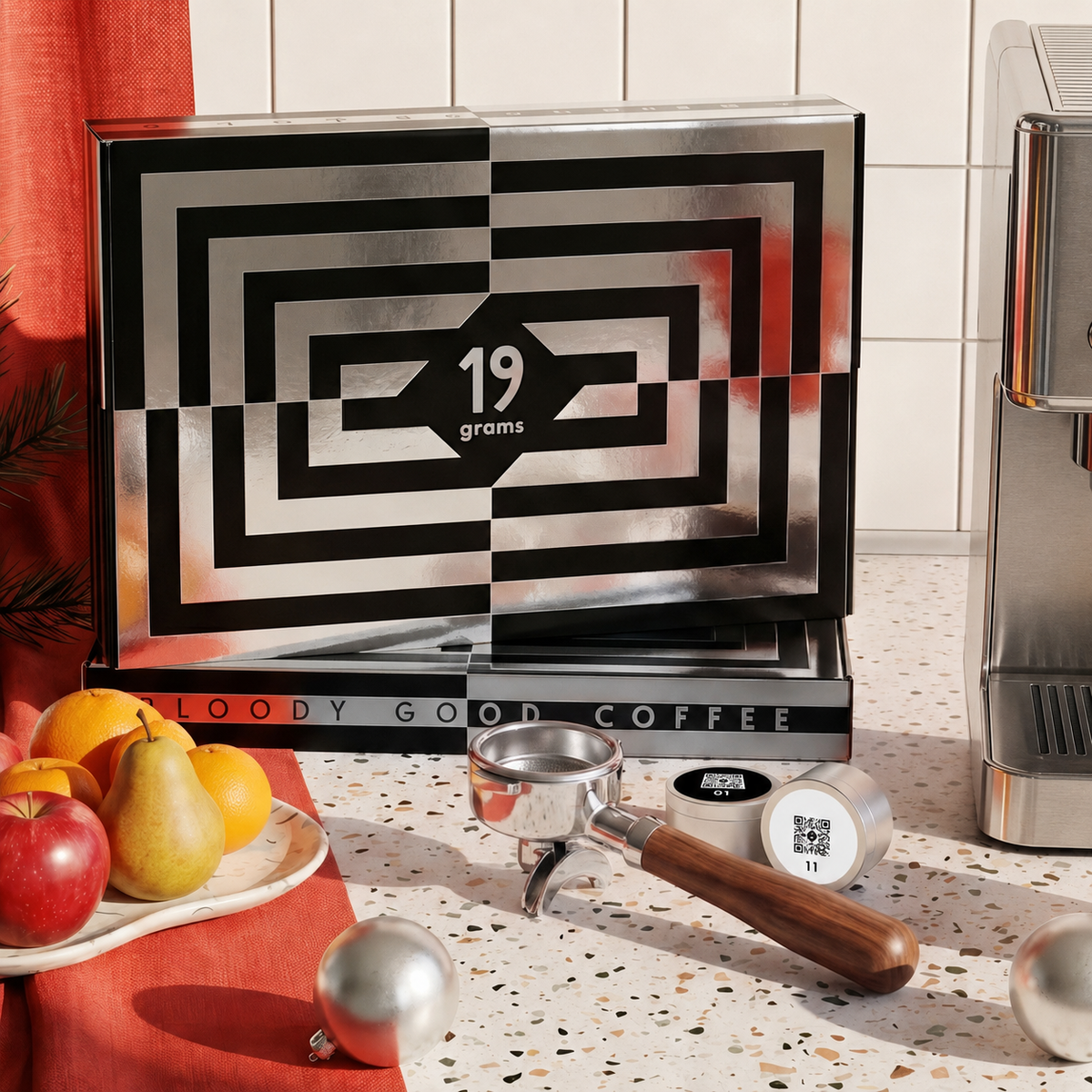 19grams Kaffee Adventskalender Espresso – Moodbild der schwarz-weiß gemusterten Kalenderbox mit Siebträger, nummerierten Kaffeedosen mit QR-Code, Obstteller und Weihnachtskugeln vor einer Espressomaschine, Kaffeerösterei Berlin