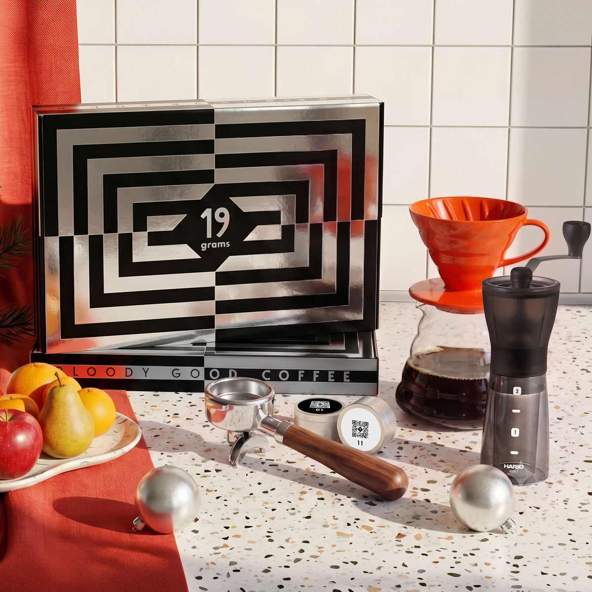 19grams Adventskalender 2026 – Moodbild der Kalenderbox mit orangem Handfilter, Hario-Handmühle, Siebträger und Kaffeedosen vor rotem Vorhang