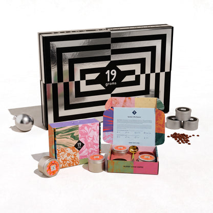 19grams Adventskalender 2026 Value Pack – Produktfoto der schwarz-weiß gemusterten Kalenderbox mit geöffneter Box, silbernen 50g-Dosen und Kaffeebohnen