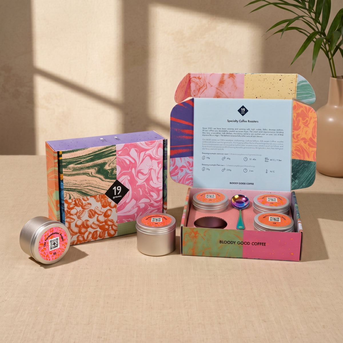 19grams The Fermentation Project Kaffee Kit Espresso – Moodbild mit geschlossener marmorierter Geschenkbox, geöffneter Kaffeebox mit vier Dosen und Löffel sowie Pflanze auf beigem Untergrund