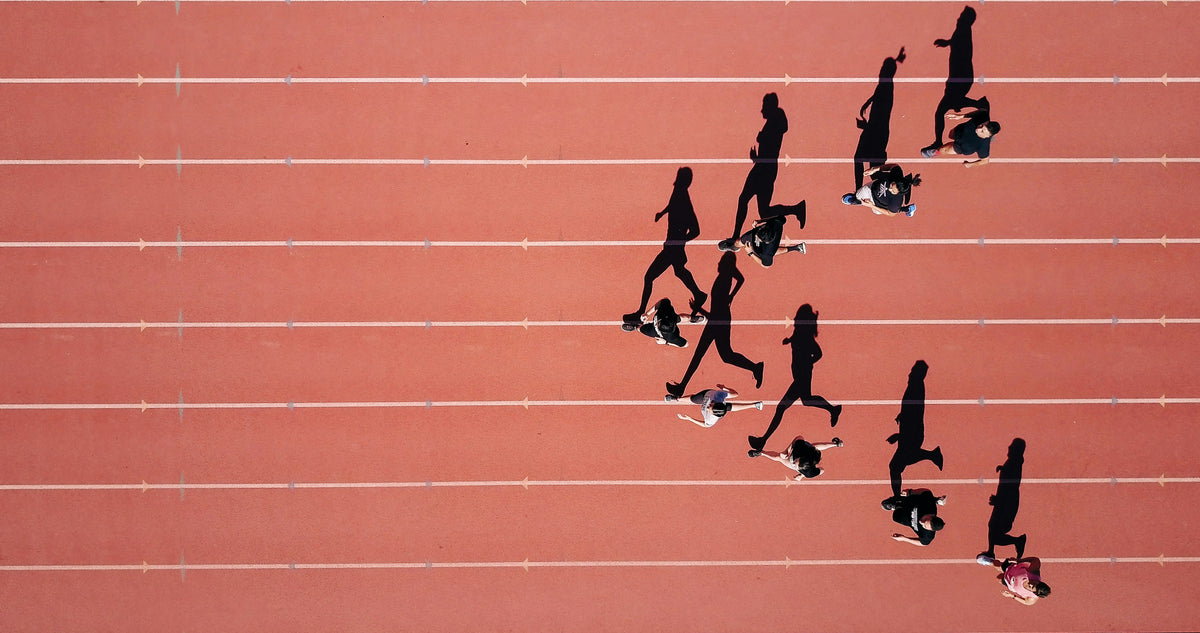 Luftaufnahme einer roten Laufbahn mit einer Gruppe Läuferinnen und Läufer und ihren langen Schatten – 19grams The Blue Line, Sonderedition zum Berlin-Marathon